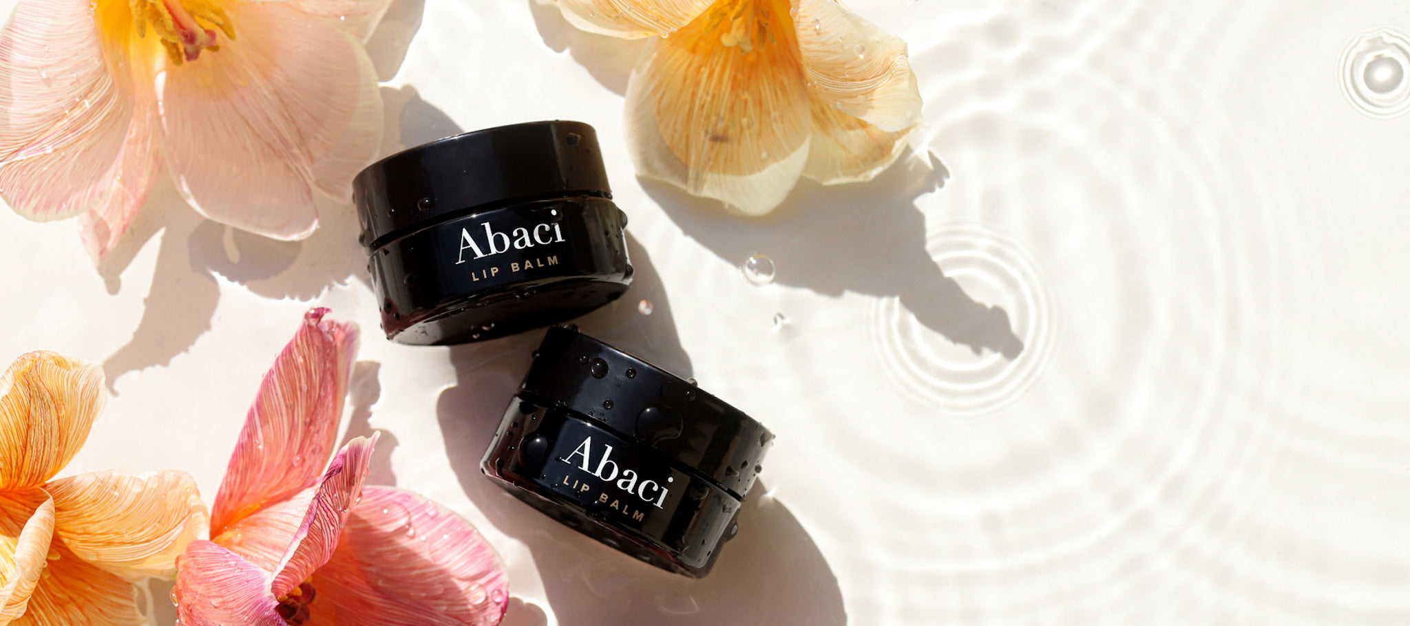 Abaci lifestyle image - Abaci Lip Balm on a background of water, surrounded by pink and orange flowers
